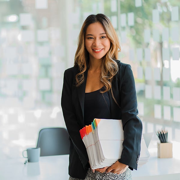 A UC online student standing in an office holding a pile of paperwork.