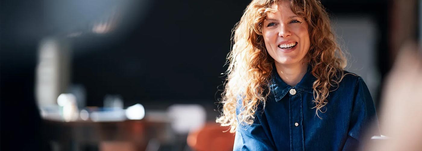 A woman smiling while seated at a table, exuding warmth and positivity.