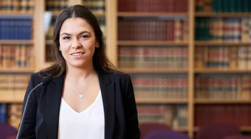 A smiling law student holds a book outside, representing the journey of becoming a lawyer in Australia.