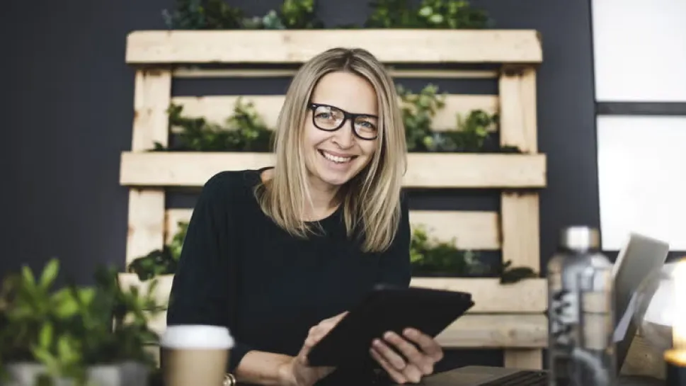 A smiling professional woman holds a tablet in a modern workspace, representing top productivity apps for working students