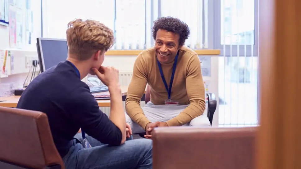 A school counsellor leans forward attentively during a one-on-one session with a young male client