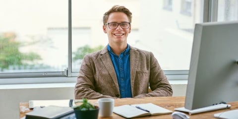 A smiling policy professional sits behind a desk in front of a computer.