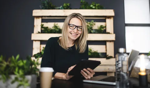 1. A woman wearing glasses is focused on using a tablet computer, engaged in her task.