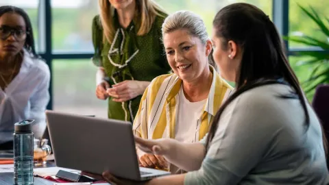Education professionals collaborate around a laptop, representing career opportunities with a Master of Education