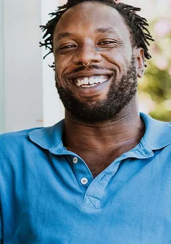 A man smiles while sitting outside, enjoying the fresh air and natural surroundings.