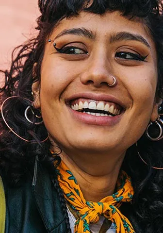 A woman with curly hair wearing a black leather jacket smiles warmly at the camera.