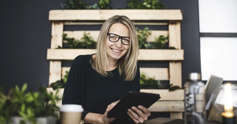 A smiling professional woman holds a tablet in a modern workspace, representing top productivity apps for working students