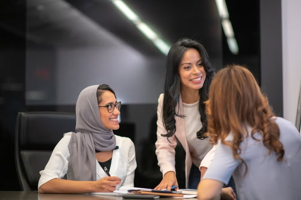 Three women professionals engage in a discussion around a table, representing what public policy is and how it works
