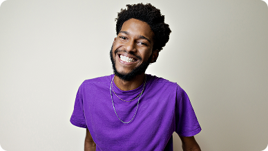 A man wearing a purple shirt smiles warmly at the camera.