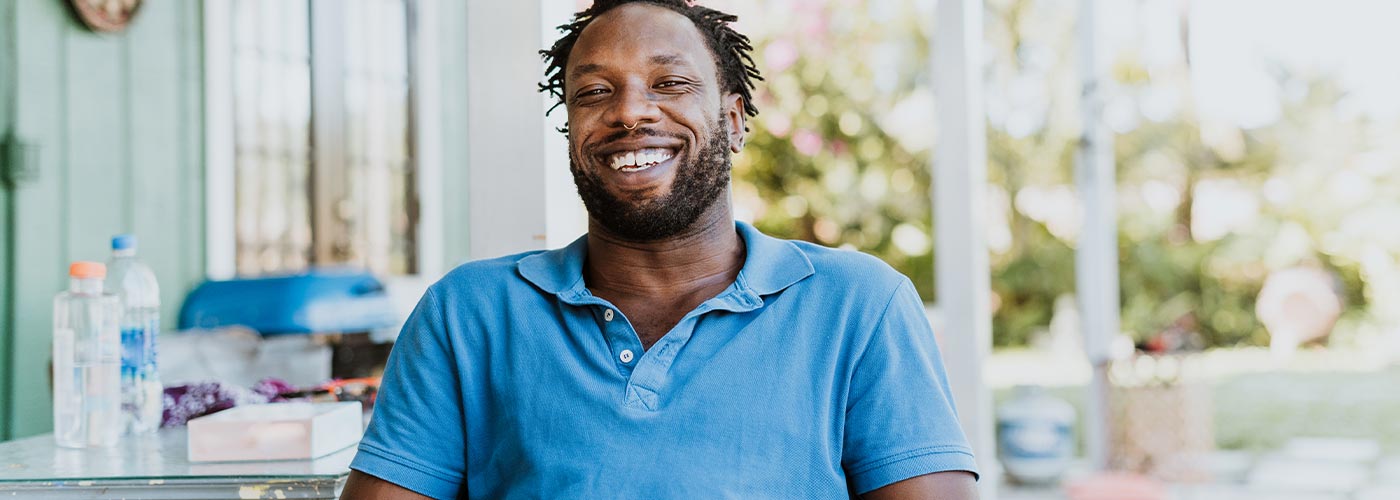 A man smiles while sitting outside, enjoying the fresh air and natural surroundings.